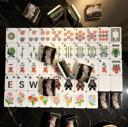 Gilded Obsidian American mahjong tiles laid out by suit with winds, bear jokers, flowers and black-and-gold marble backs