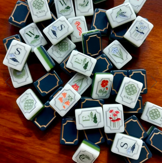 Kensington Coast American mahjong tiles scattered on a wooden table, with navy and gold backs and white botanical faces