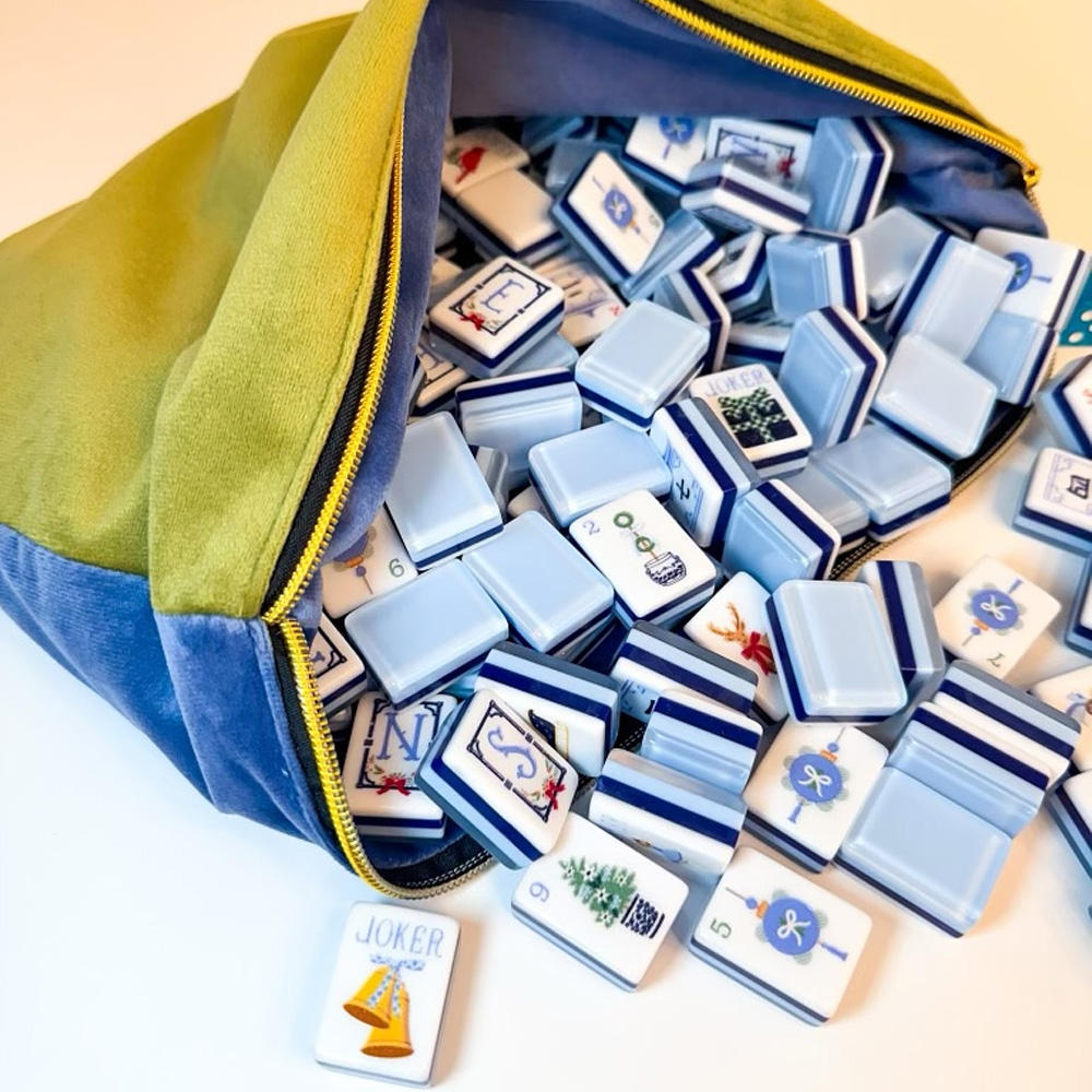 A blue and olive green zippered bag spilling out many small rectangular game pieces with blue and white stripes, numbers, and illustrated symbols, photographed on a clean white background.