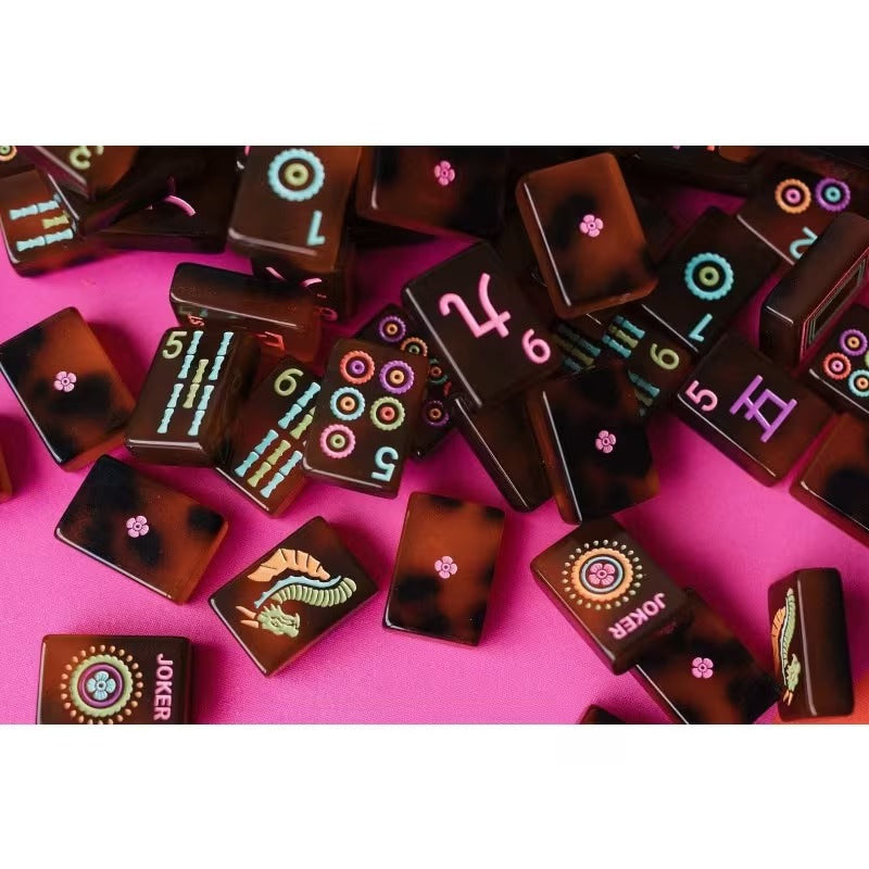 Amber tortoiseshell American mahjong tile pile with two Joker tiles and colorful painted symbols on pink background - glossy dark-brown marbled tiles ideal for hostess and collector gifts