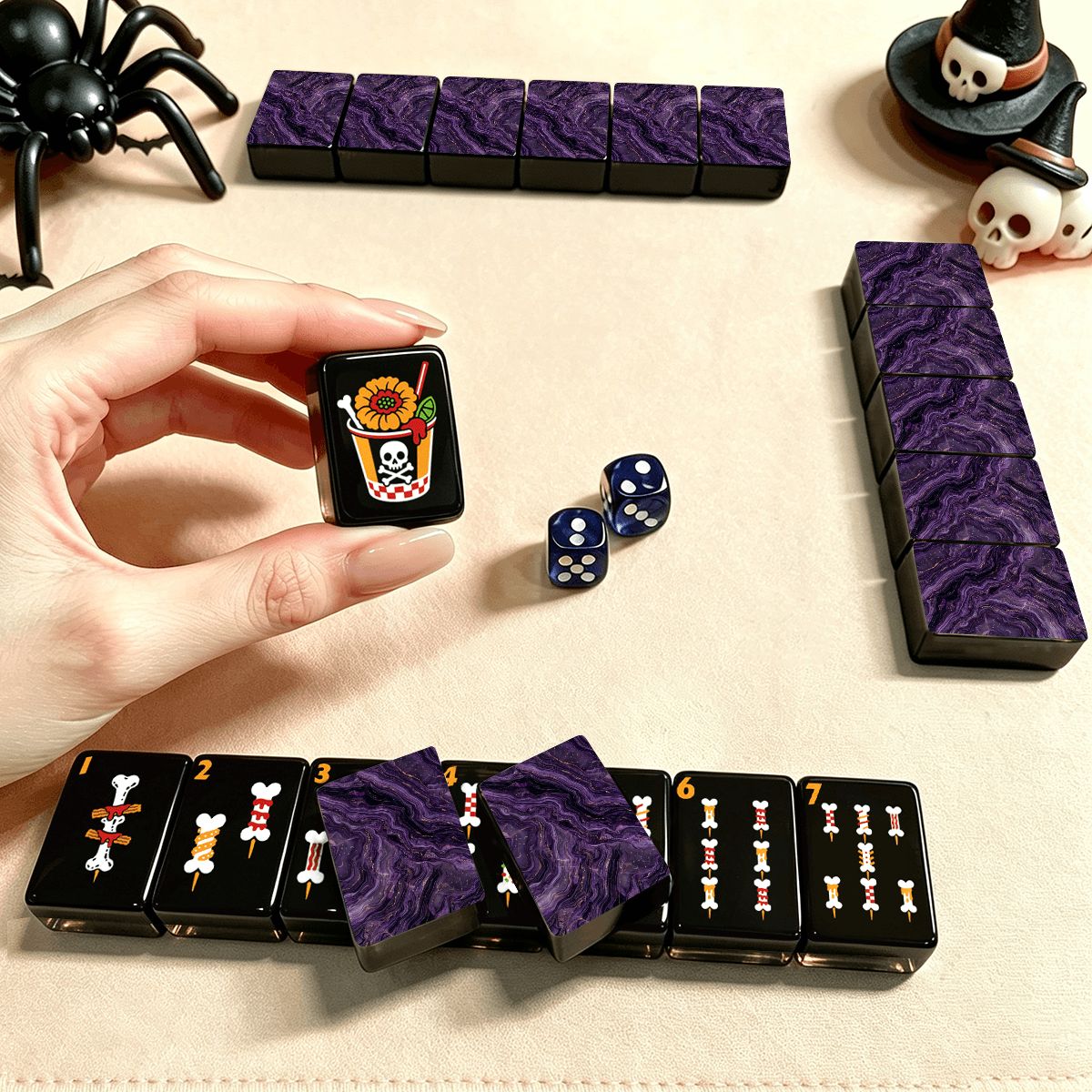 Hand holding a Skull Diner Halloween mahjong tile with ghost boba drink illustration, purple marble tiles and dice in play on tabletop